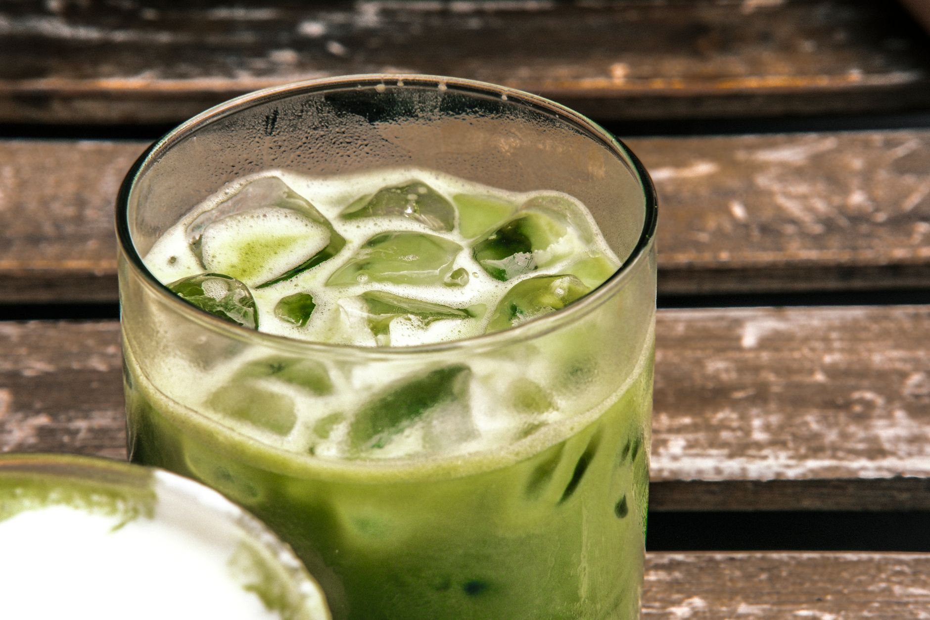 A close-up of a refreshing iced matcha latte on a rustic wooden table, highlighting its natural green color and fresh appeal.