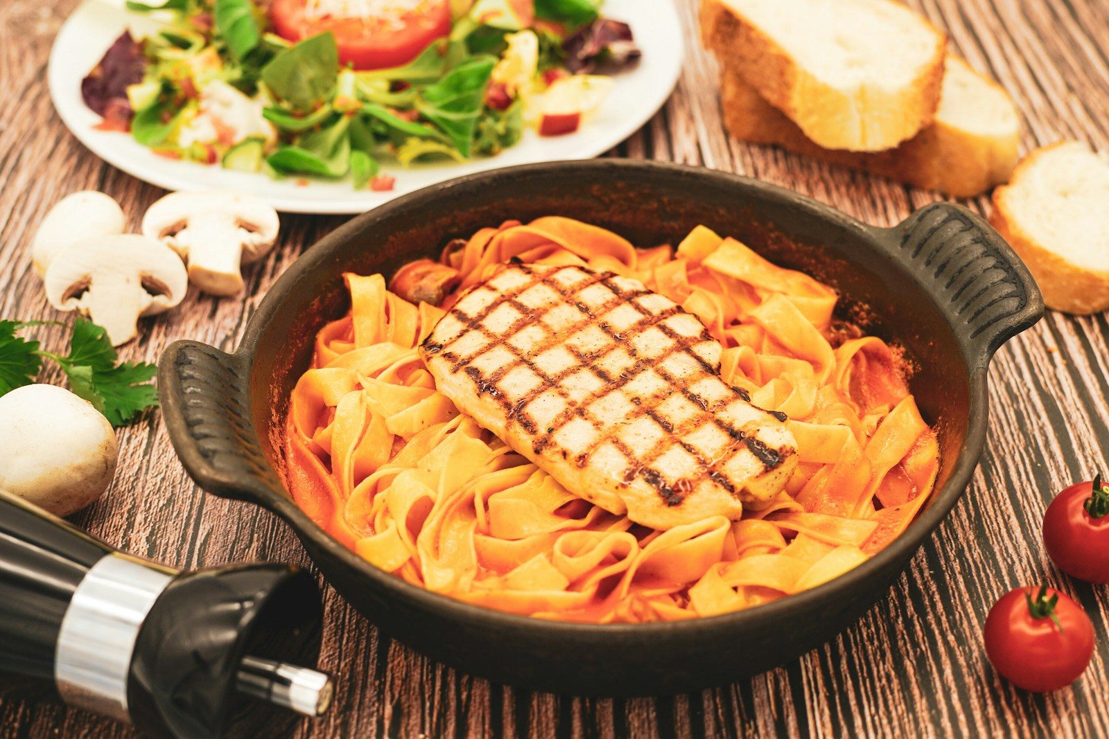 Grilled chicken pasta, fresh salad, bread, and wine on table