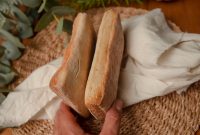Close up of hands holding ciabatta bread on a rustic table setup with greenery.