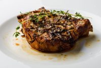Delicious herb-crusted pork chop served on a white plate, garnished with fresh thyme.