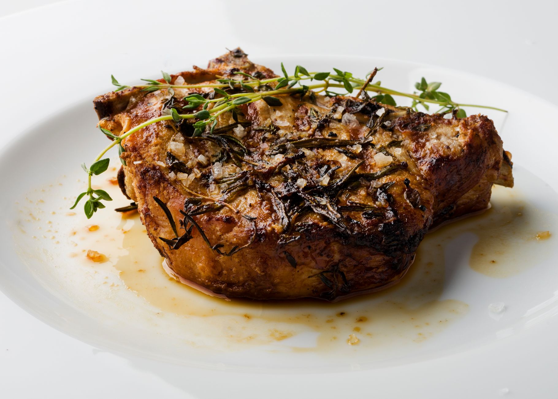 Delicious herb-crusted pork chop served on a white plate, garnished with fresh thyme.