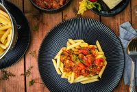 aap-easy-one-pot-vegetarian-dinners-for-busy-families-1790847099 Delicious Italian pasta with hearty tomato sauce served on a dark plate, styled as a flat lay.