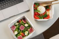 aap-healthy-lunch-box-ideas-for-office-workers-1790853960 Top view of a desk setup with two fresh salads and a laptop, ideal for a healthy office lunch.