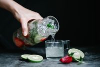 Close-up of a refreshing lime and strawberry infused drink being poured from a pitcher into a glass.