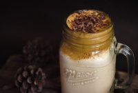 Delicious creamy dalgona coffee topped with chocolate shavings in a mason jar, perfect for a cozy indoor setting.
