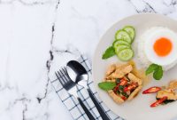 A close-up photo of a Thai meal featuring chicken, rice, and a fried egg.