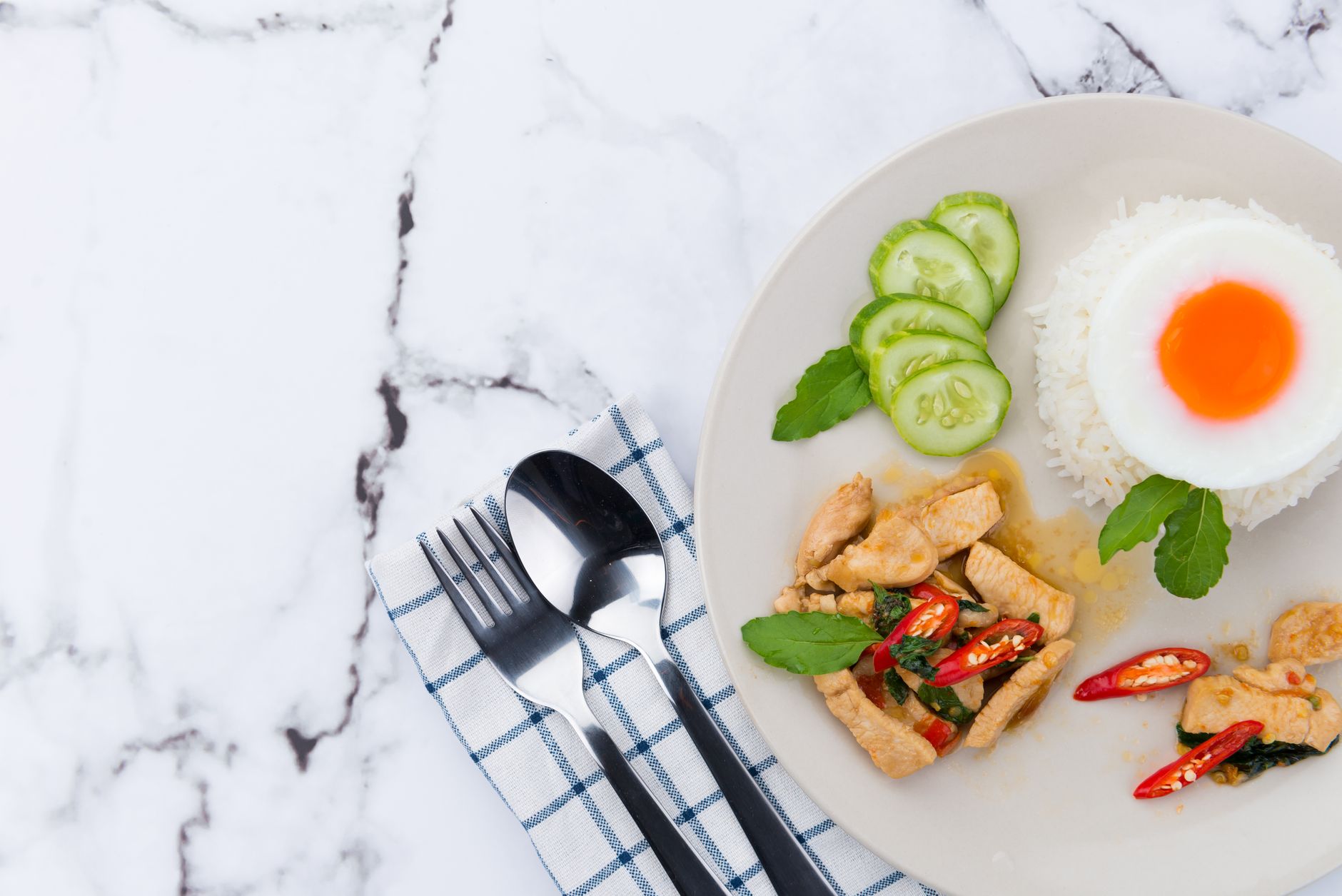 A close-up photo of a Thai meal featuring chicken, rice, and a fried egg.